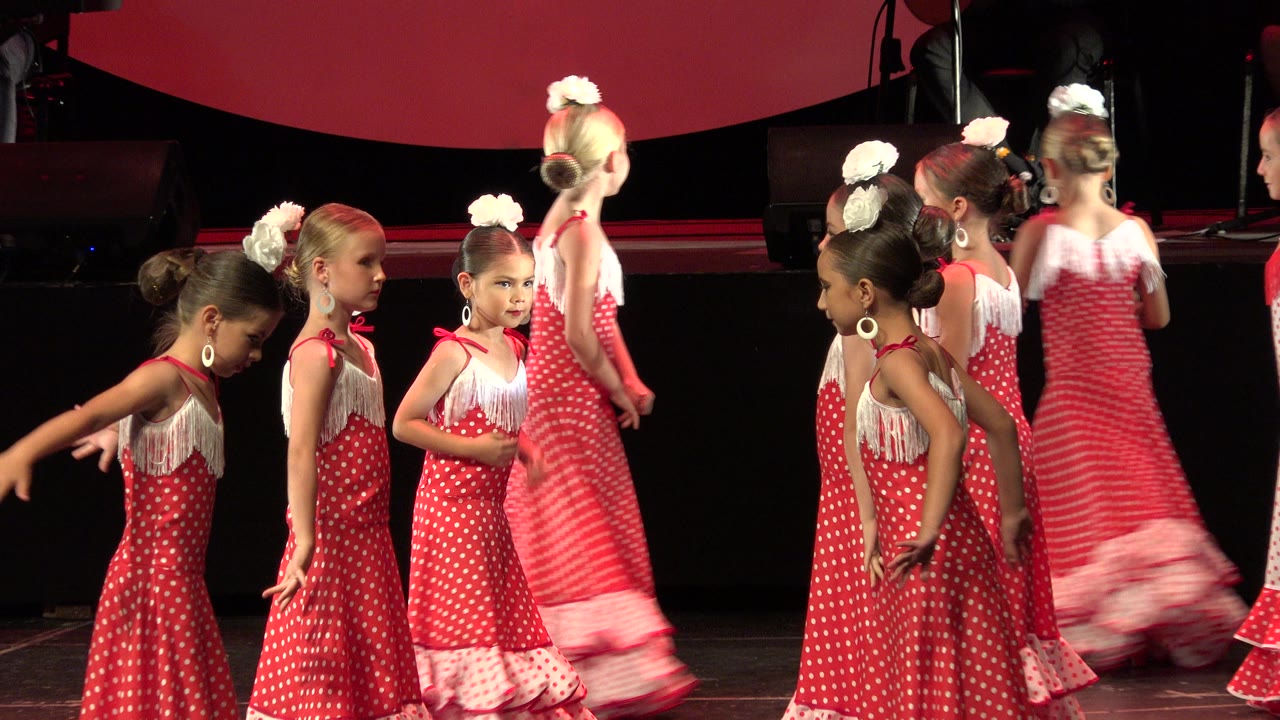 Children in matching red dance costumes move on stage.