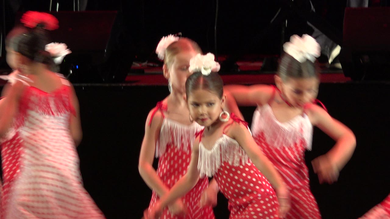 Girls in red and white dresses dancing on a dark stage.