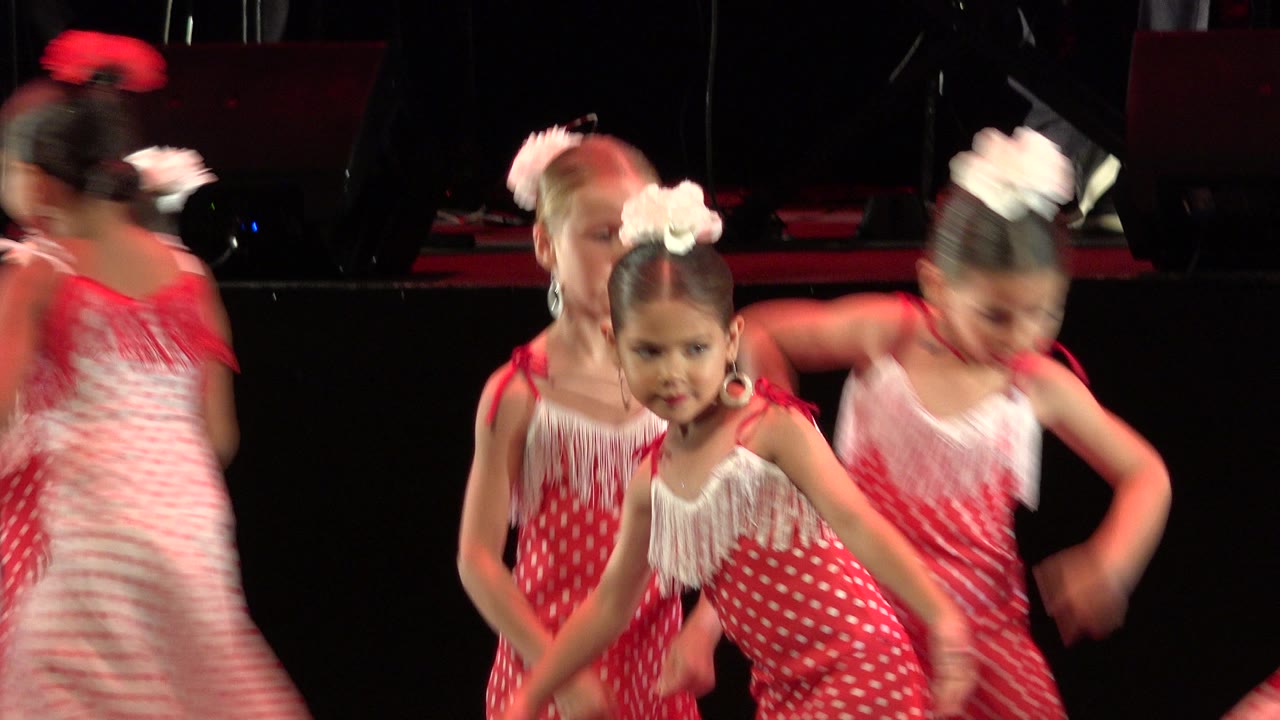 Three young girls in matching red and white dresses dance close together on the stage in Cabo San Lucas, Mexico, with the center child facing the camera.