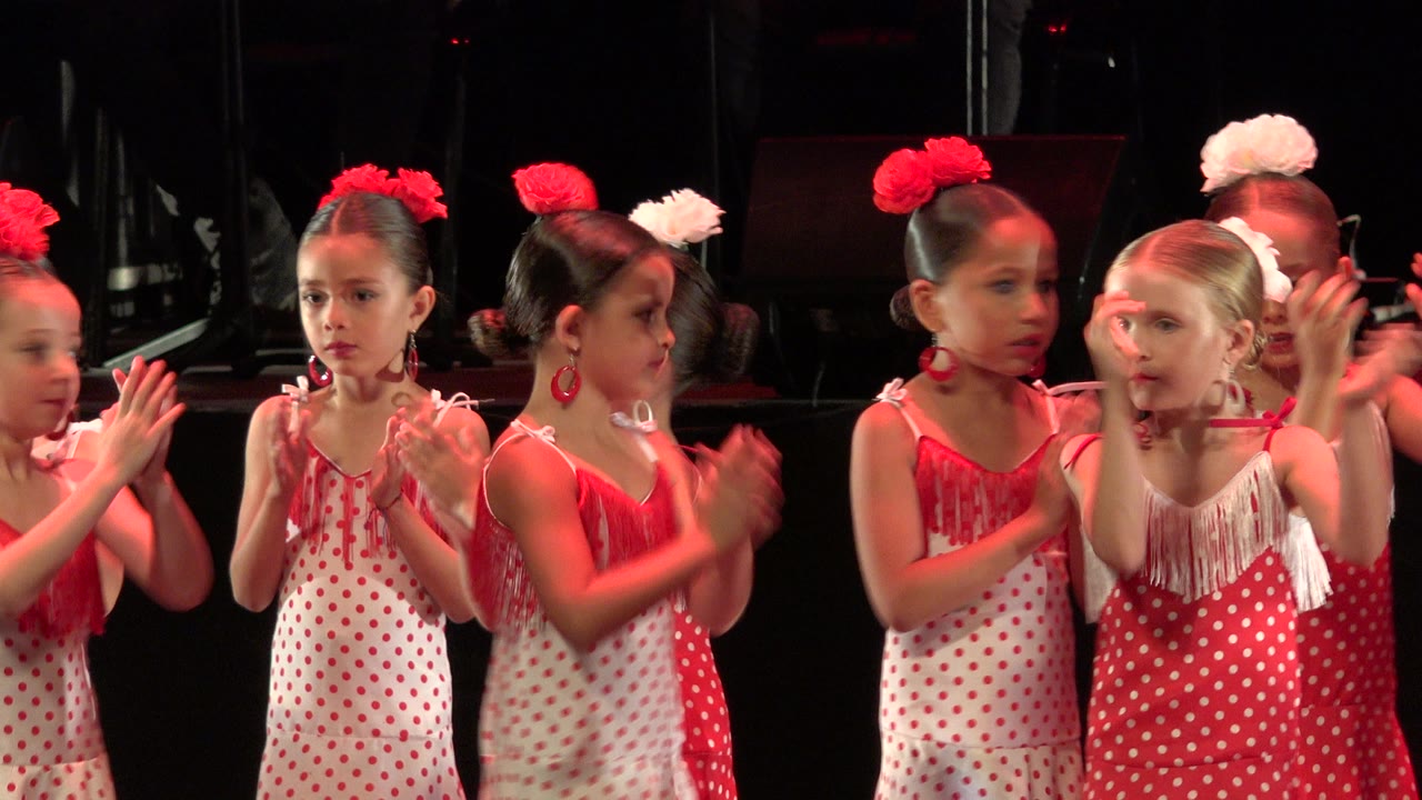 Several girls in matching red and white costumes clap and look across the stage during the Cabo San Lucas performance.