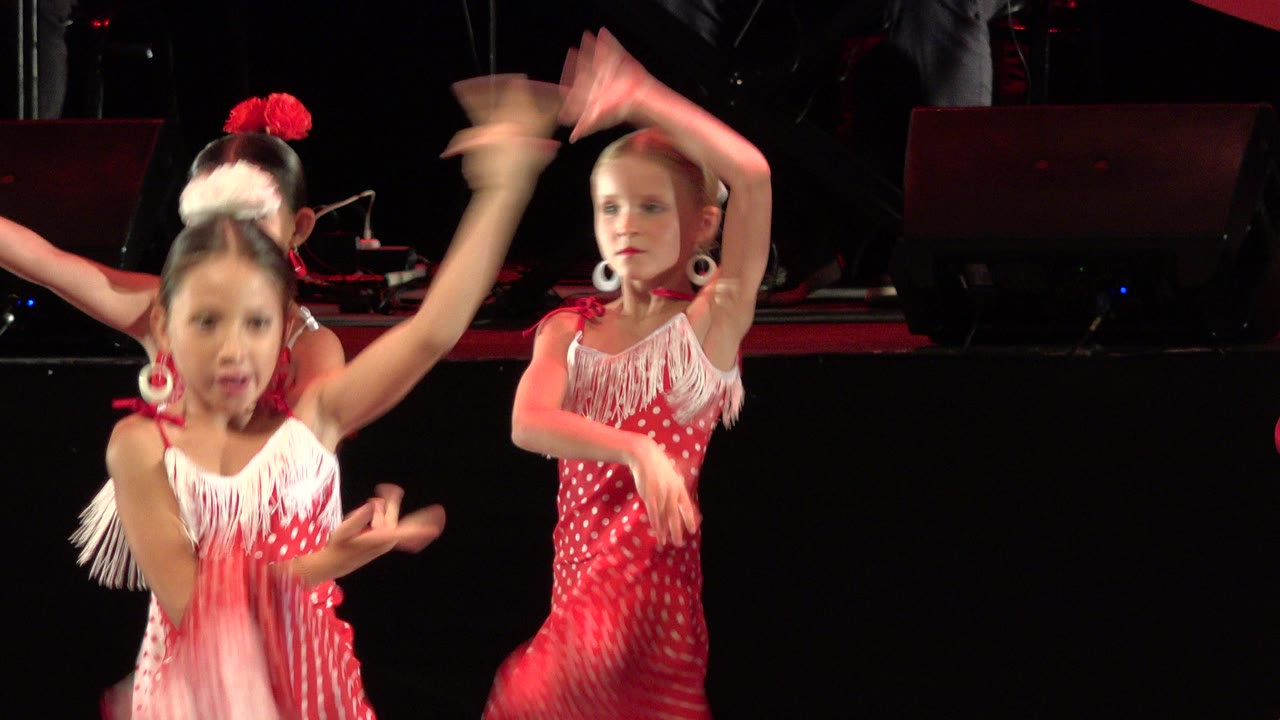 The dancers continue the routine in Cabo San Lucas, Mexico, with motion-blurred hands, white fringe, and red polka-dot costumes against a black stage background.