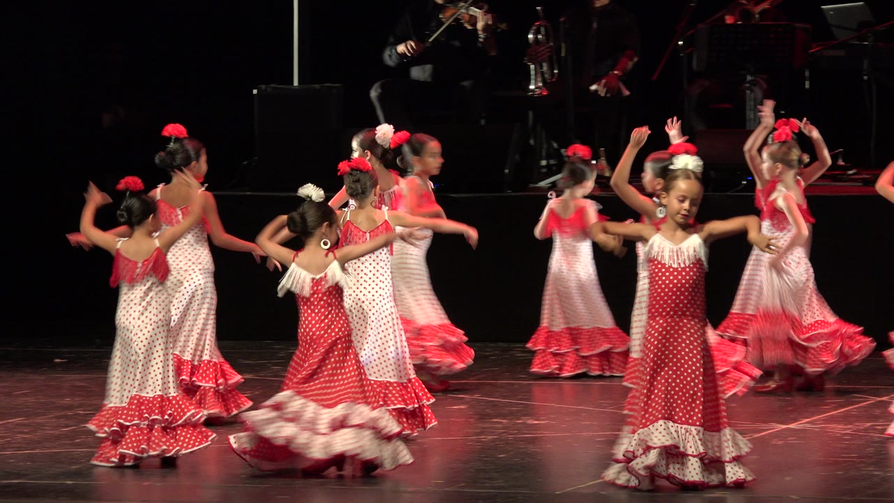 Girls in pink and white dresses dancing on a dark stage.