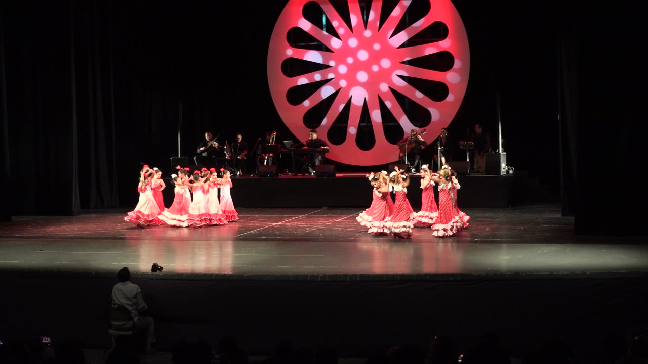 Girls in matching dresses dance in two groups on a wide stage.