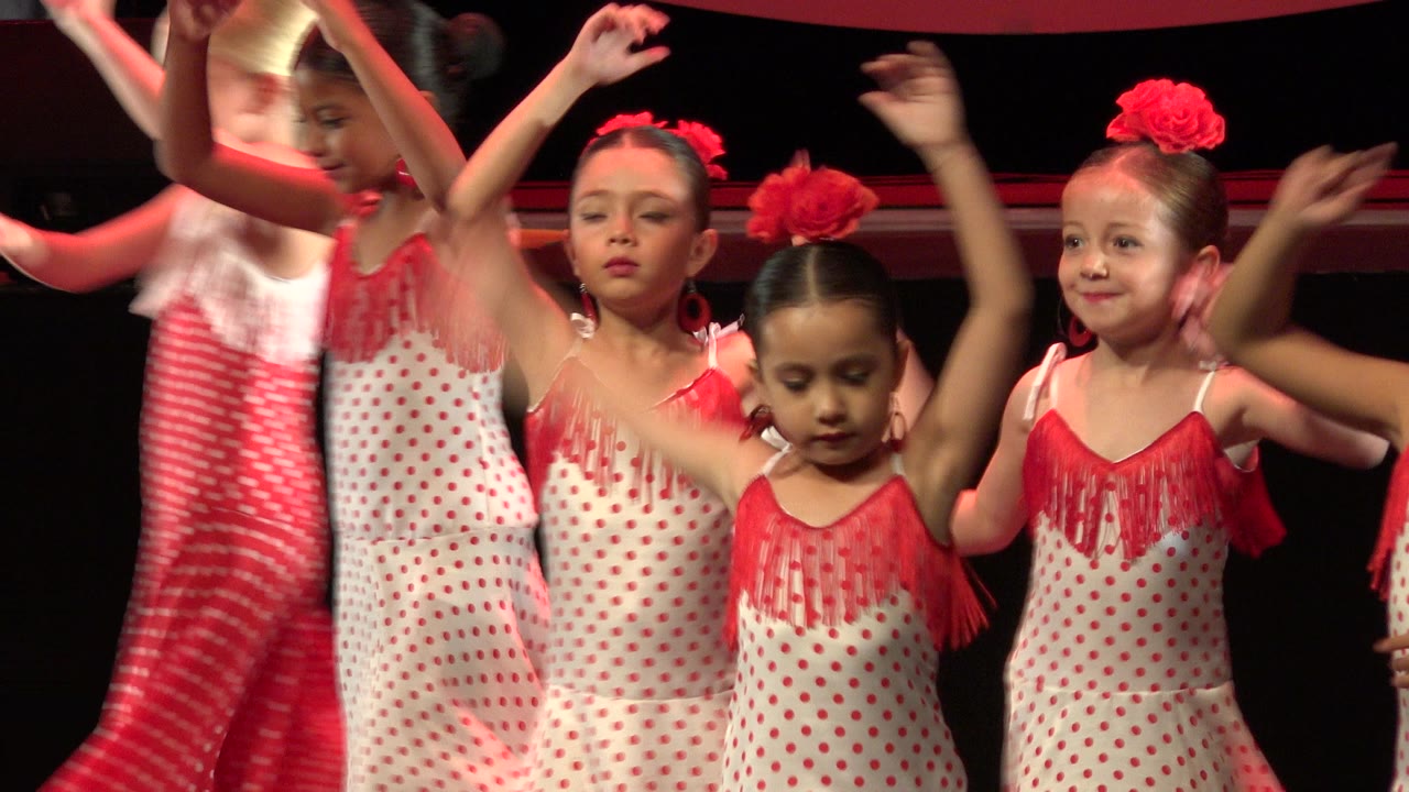 Children in red and white costumes dancing on a dark stage.