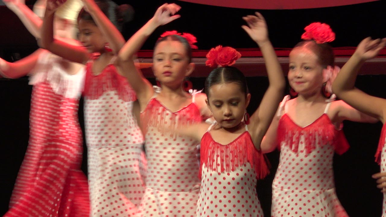 Young dancers in matching red and white outfits continue the stage routine in Cabo San Lucas, Mexico, with one child centered and others partly blurred by movement.