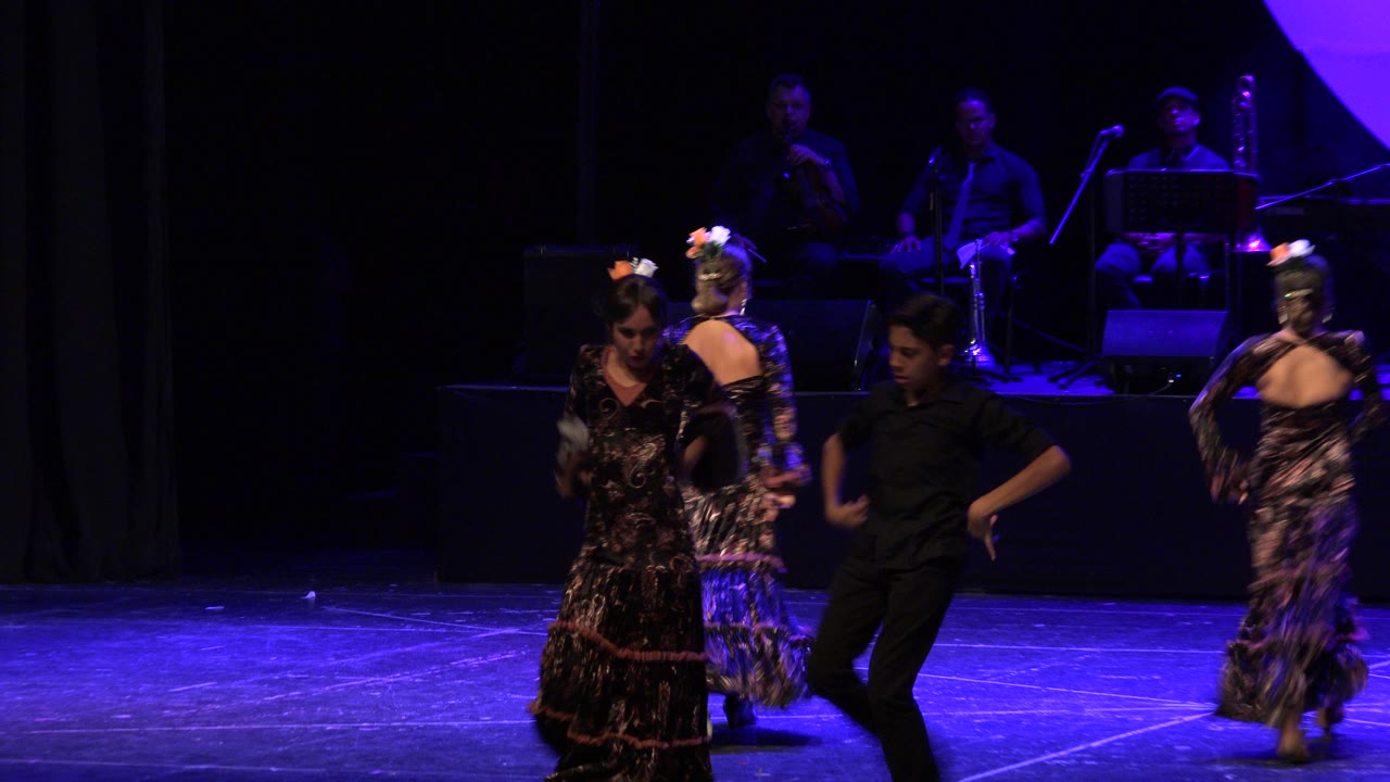 At 0:01, the dancers shift positions across the Cabo San Lucas stage while the band remains visible in the dark background under purple-blue light.