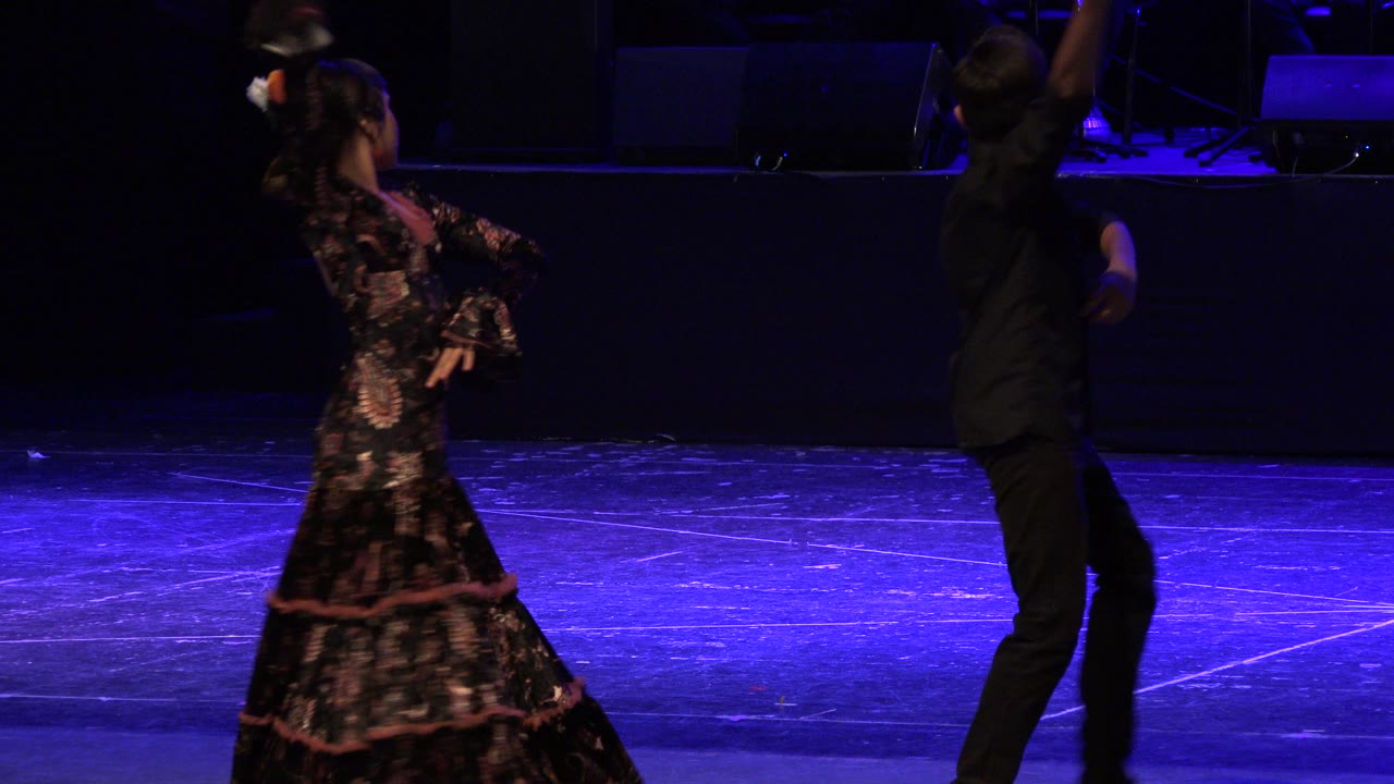 At 0:01, the girl leans back with one arm raised while the boy faces her from the right side of the Cabo San Lucas stage.