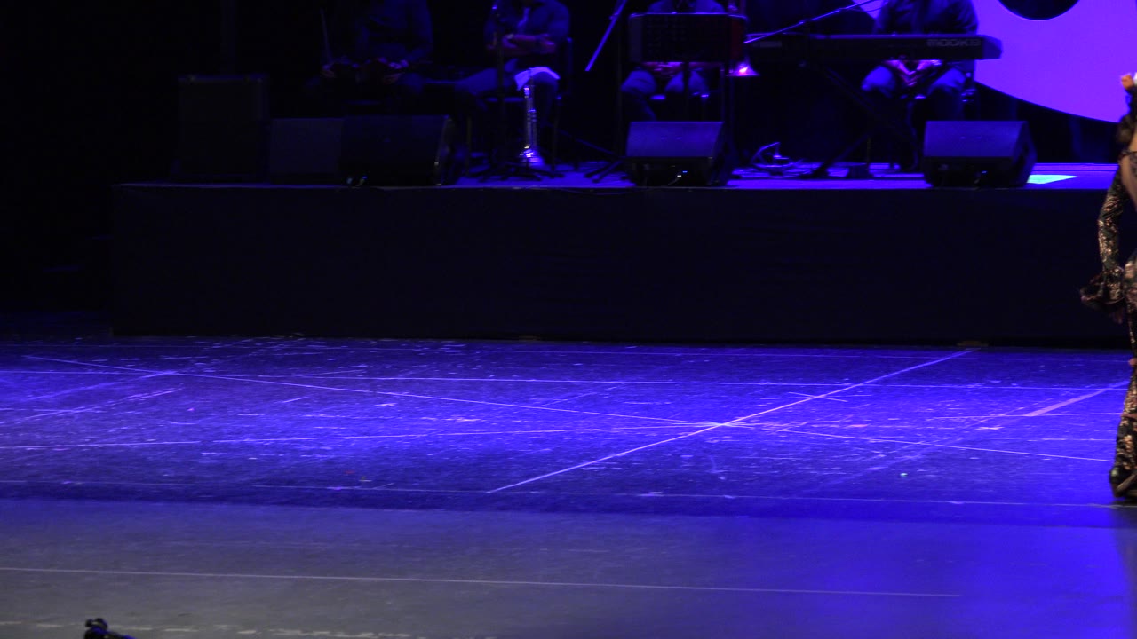 Blue-lit stage with musicians and a partial dancer at the right edge.