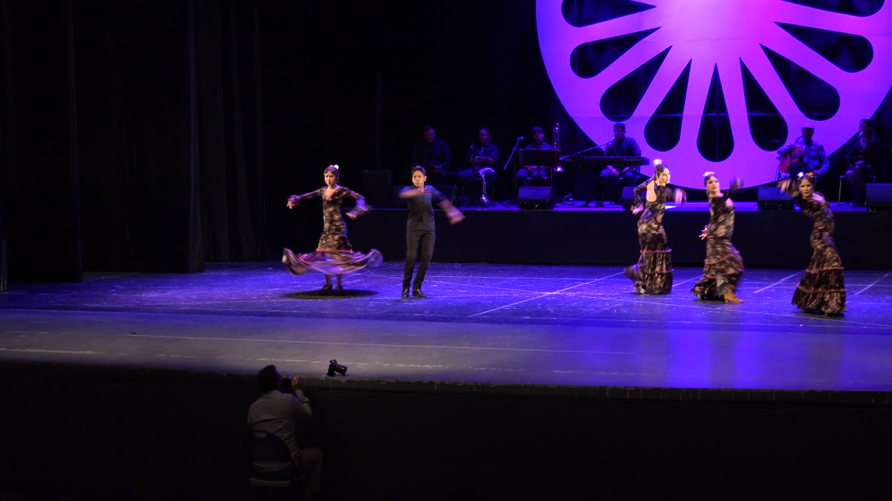 Dancers shift across a stage with a bright circular backdrop.