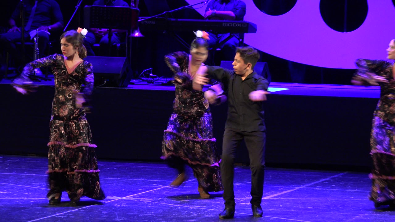 Children dancing on a blue-lit stage with musicians in the background.