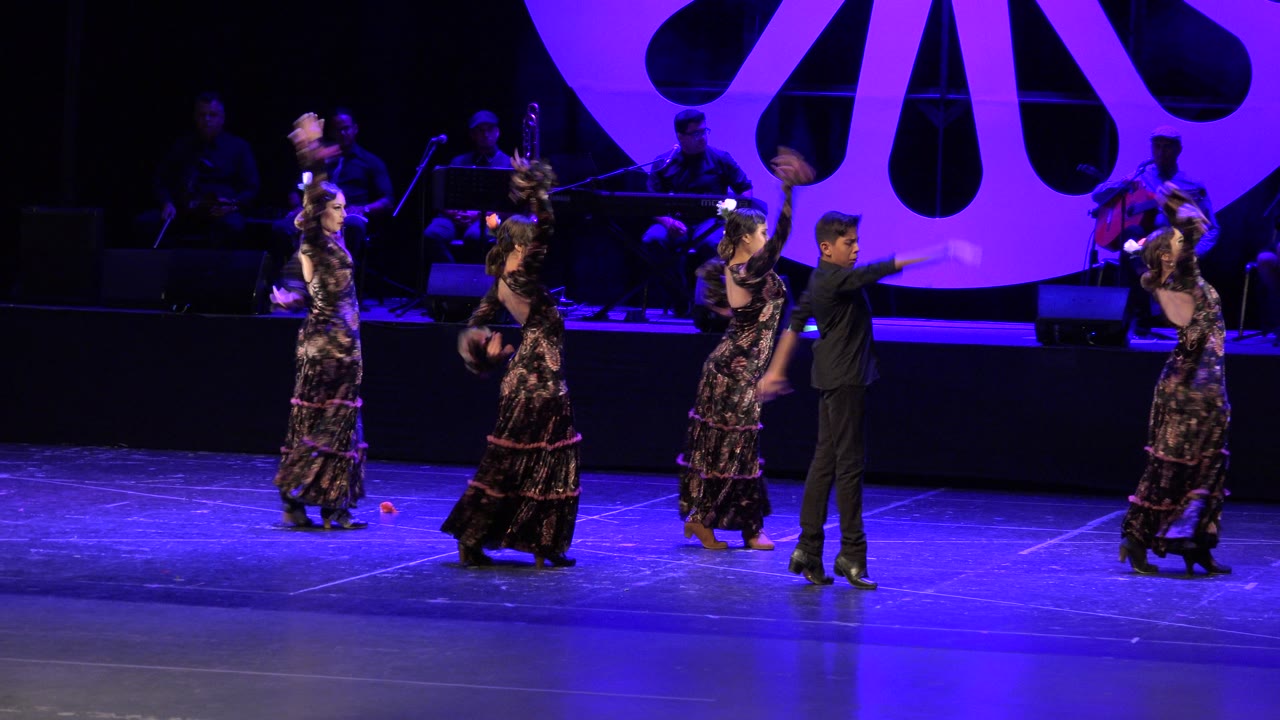 Dancers raise fans or hands during a stage performance.