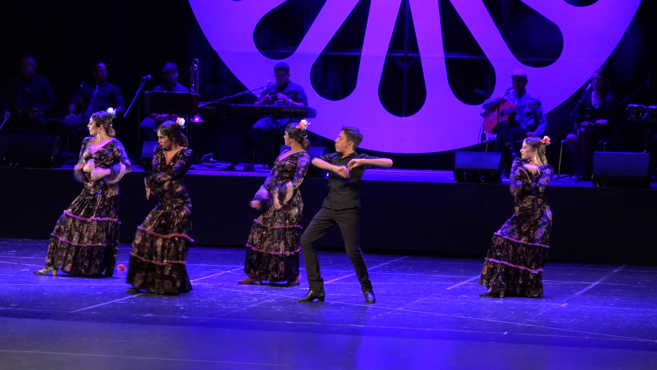 Stage dancers under purple and blue lighting with musicians in the background.