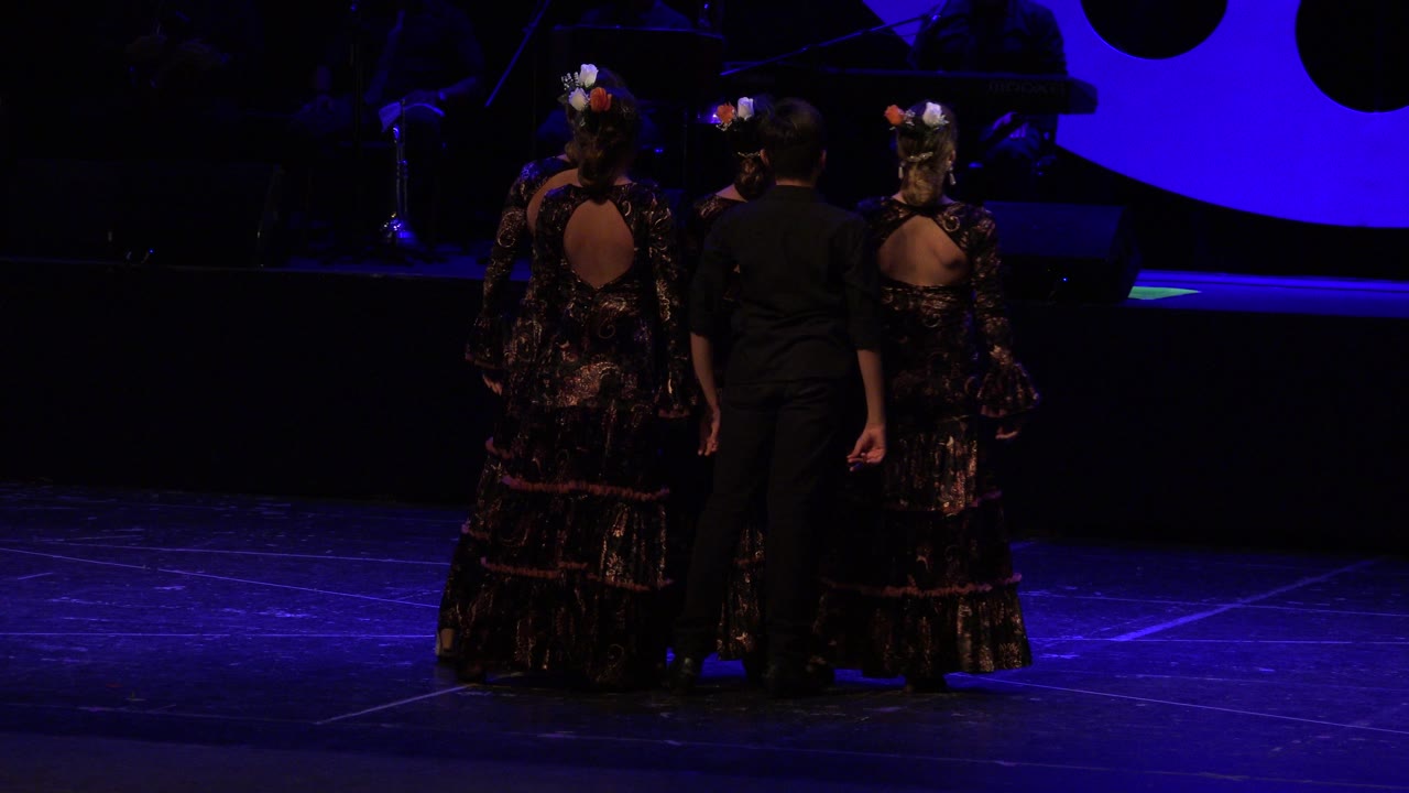 Three performers seen from behind on a blue-lit stage.