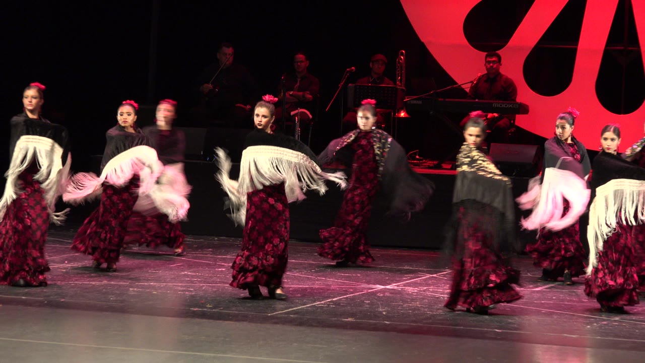 Women dancers perform on a dark stage with musicians behind them.