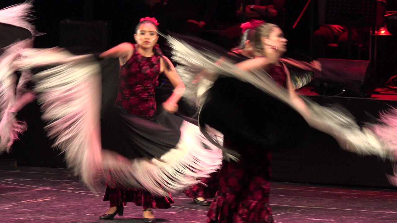 One second into the Cabo San Lucas clip, the young dancer remains centered as sweeping black and white shawl fabric fills the foreground and a second performer blurs at right.