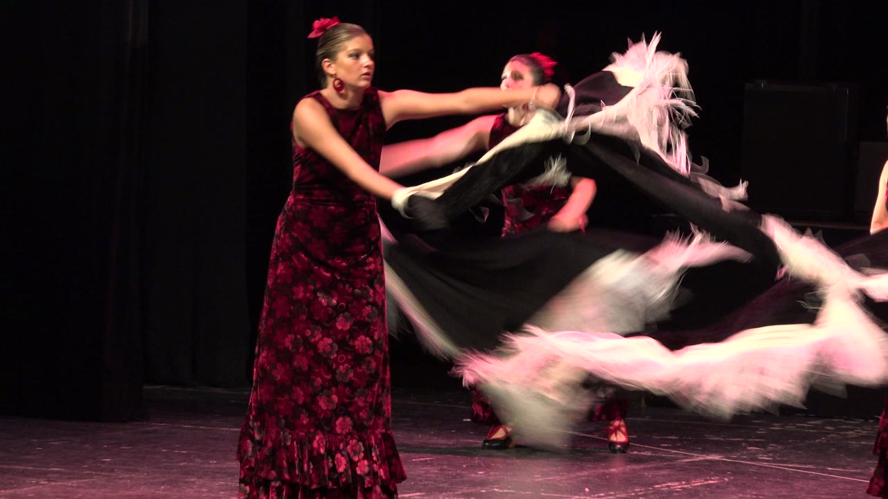 Women and girls on a dark stage swing fringed scarves.
