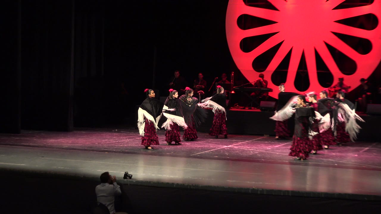 Dancers perform on a stage beneath a red circular set piece.