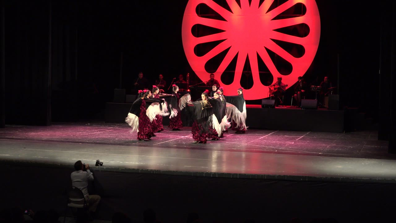 Dancers in red, white, and black costumes perform on a theater stage.