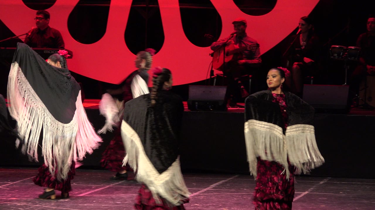 The Cabo San Lucas stage performance continues as dancers swing black shawls with white fringe, with guitar players and percussion visible on the rear platform.