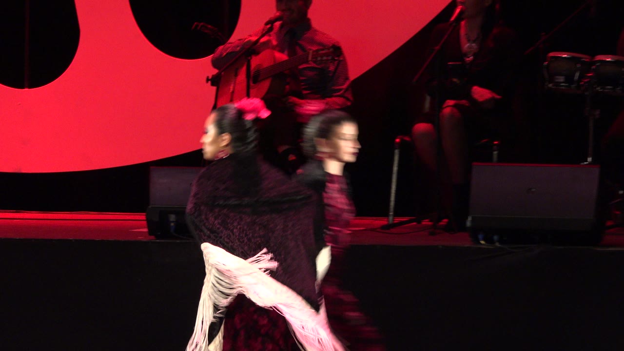 Two dancers crossing a red-lit stage with musicians behind them.