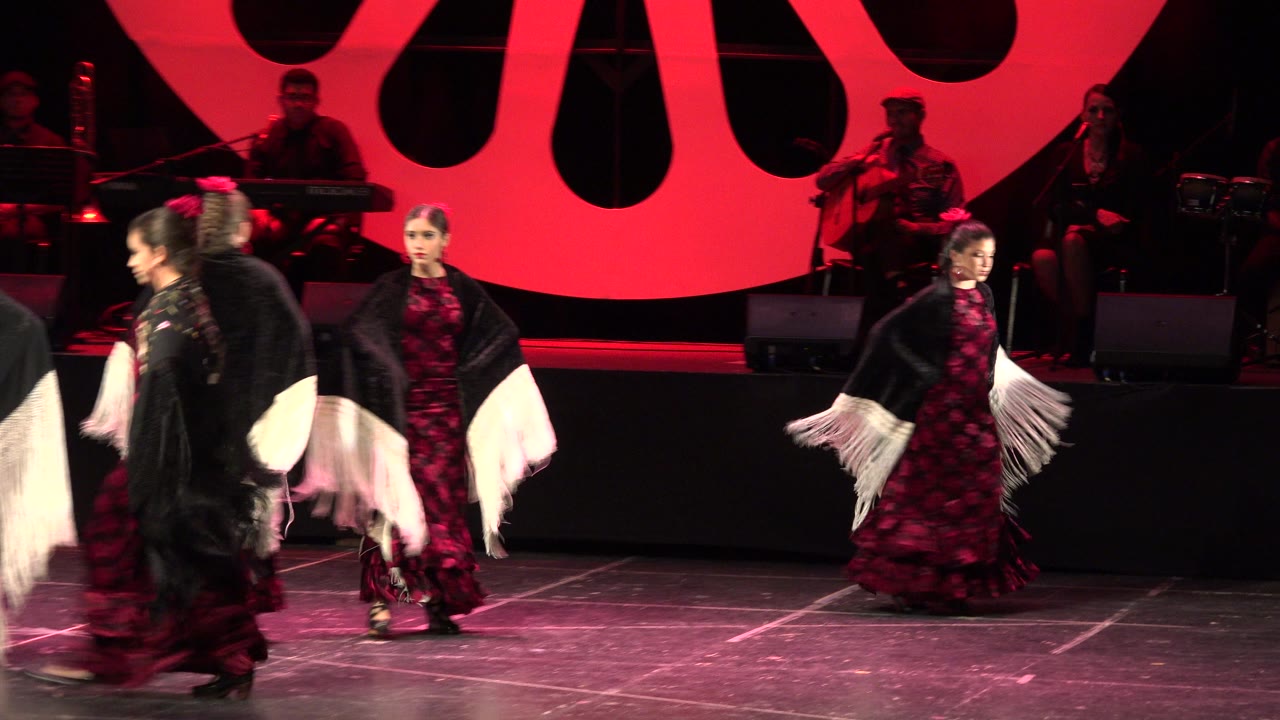 Dancers in red and black costumes perform on a stage with a red backdrop.
