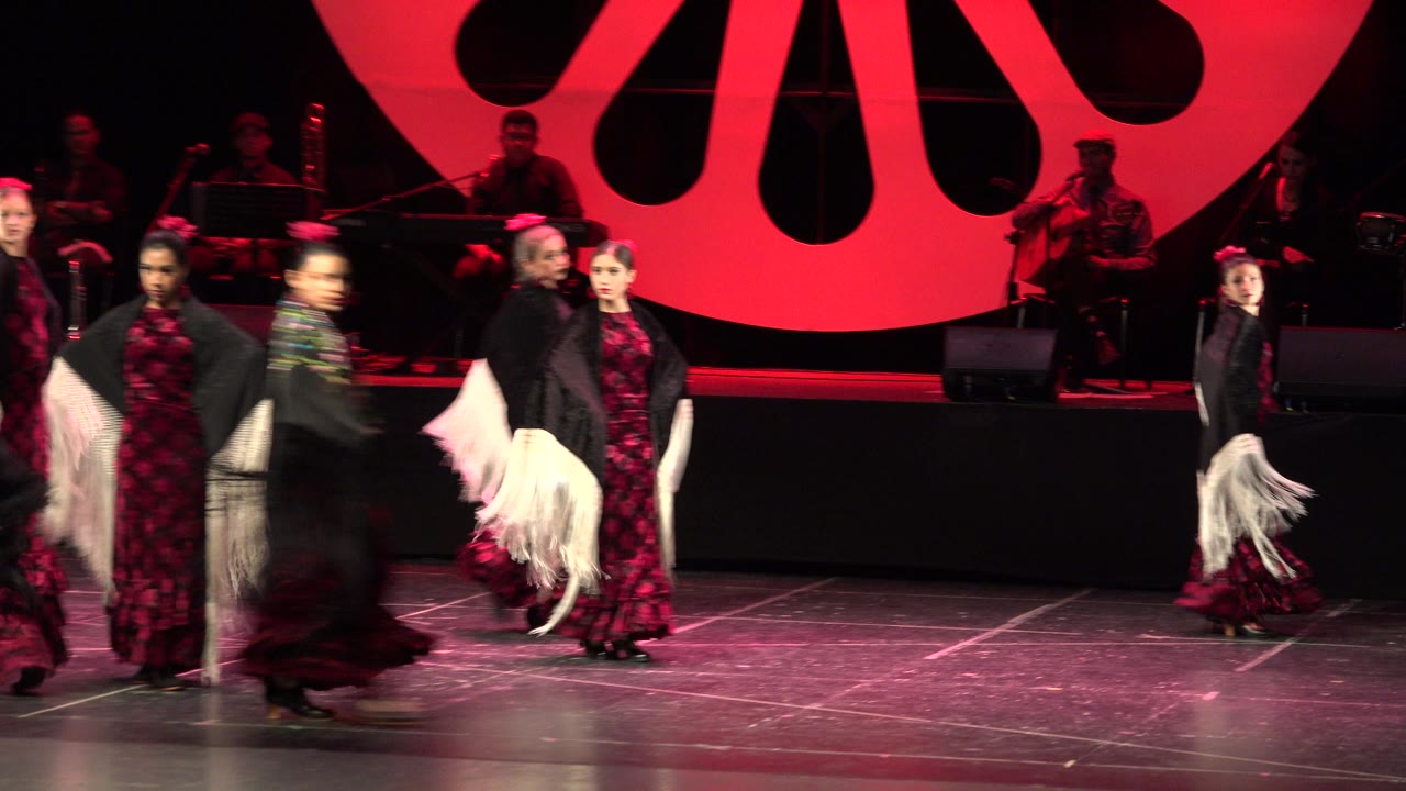 Dancers cluster near center stage during a red-lit performance.