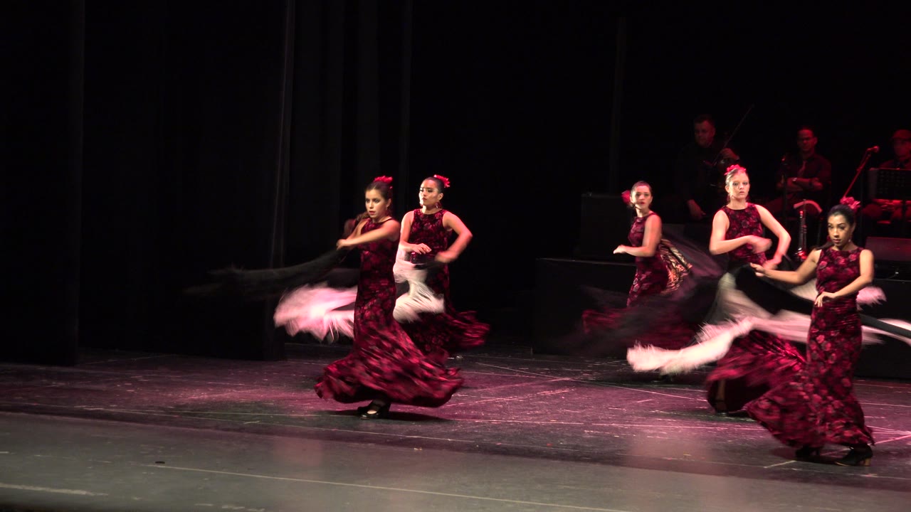The dancers continue their stage routine in Cabo San Lucas, Mexico, with two women forward and others behind them under dim theater lighting.