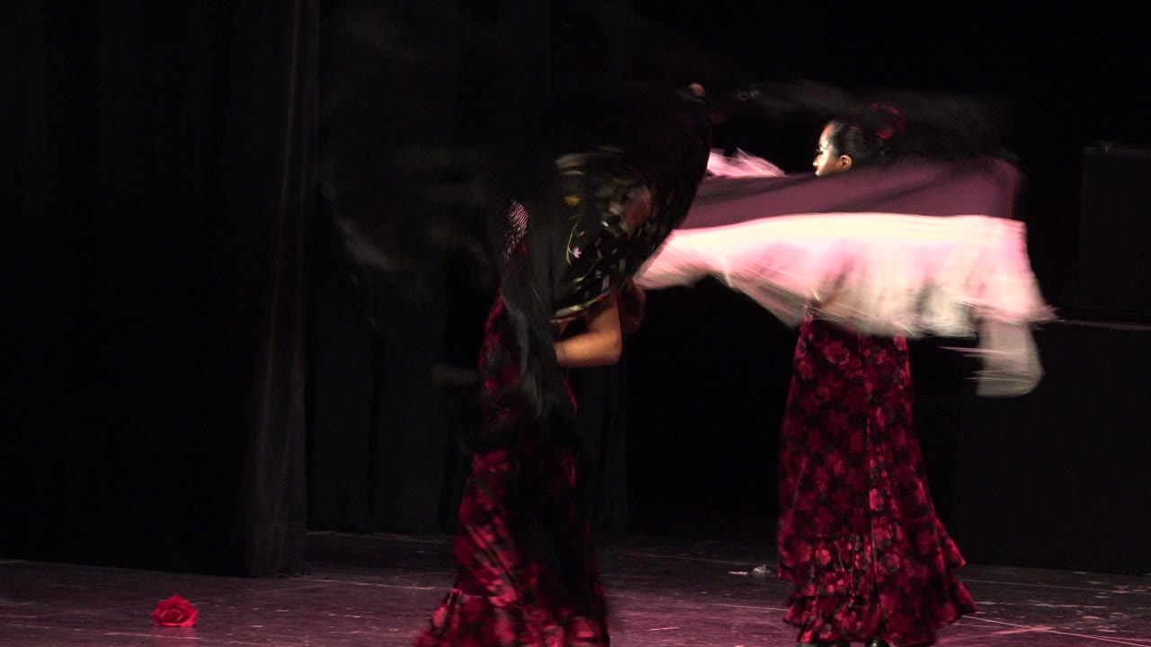 Two women dancing on a dark stage with blurred shawls.