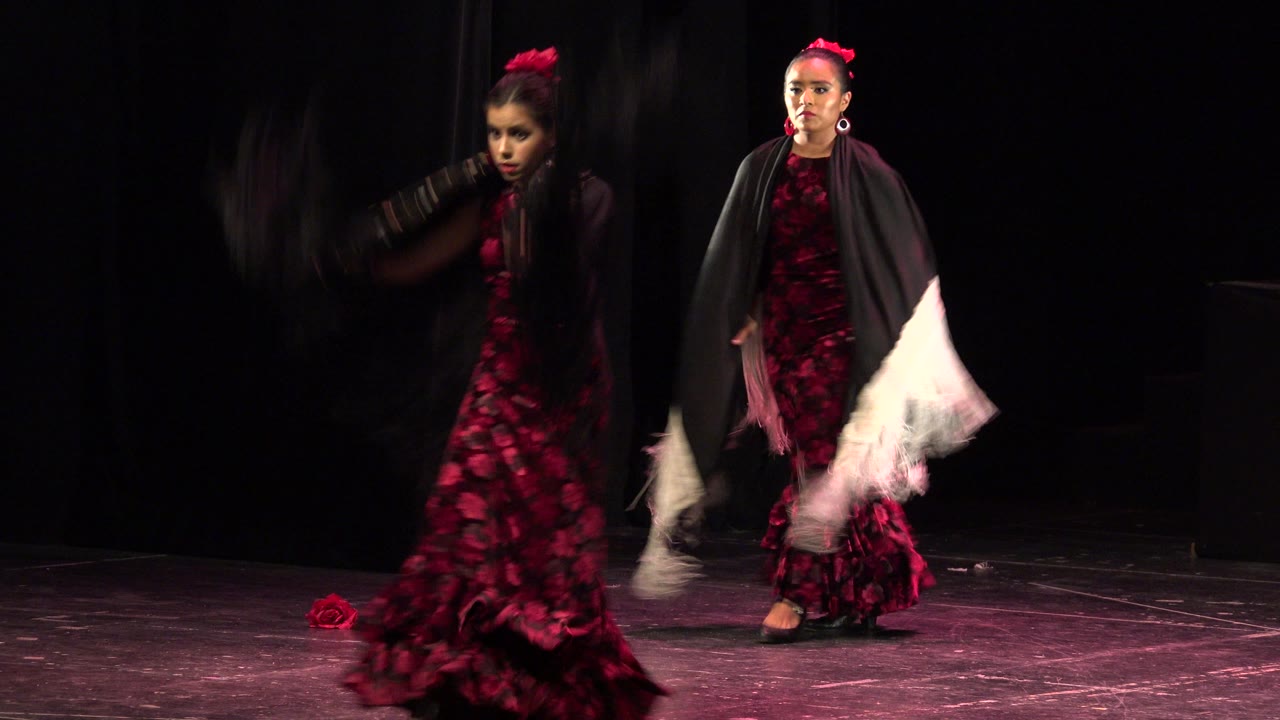 Two young dancers in red dresses perform on a dark stage.