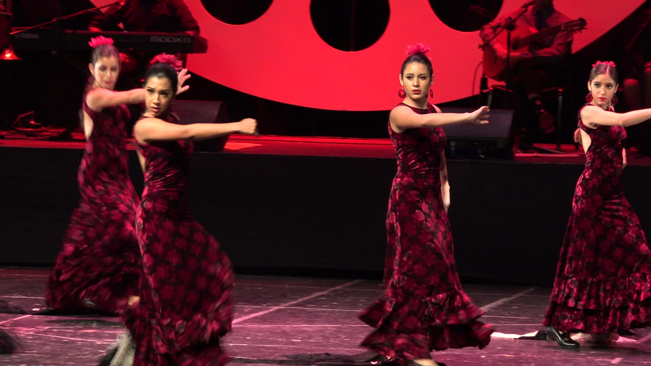 Young dancers in red dresses pose on a red-lit stage.