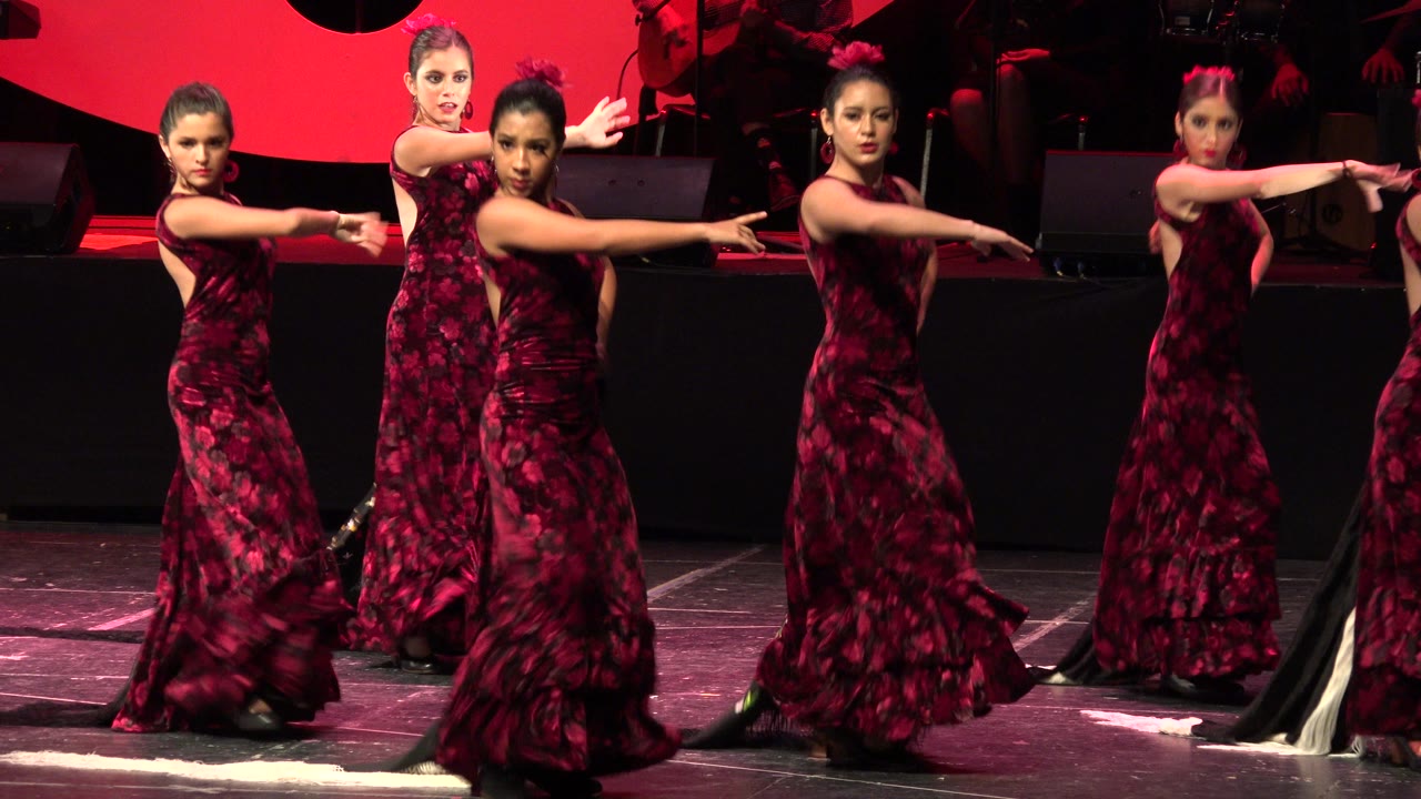 In Cabo San Lucas, Mexico, the maroon-dressed dancers remain in a tight stage formation with one performer closer to camera and others aligned behind her.