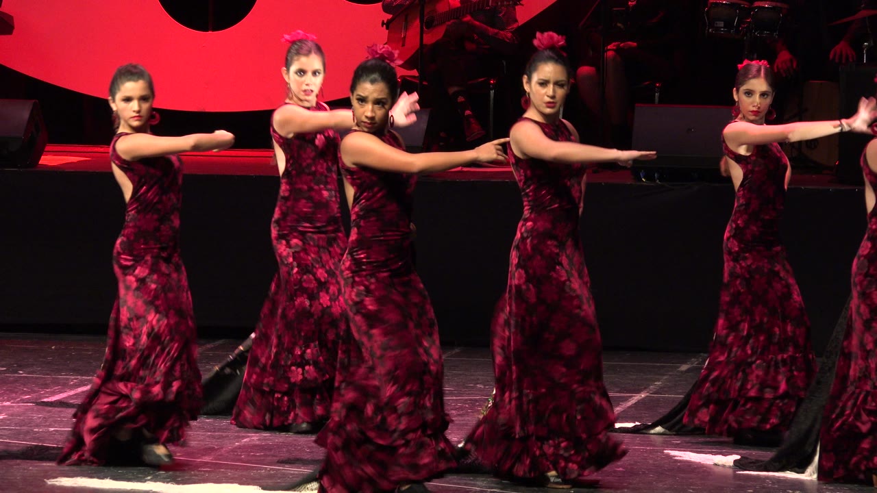 Dancers in matching maroon dresses extend their arms across the stage.