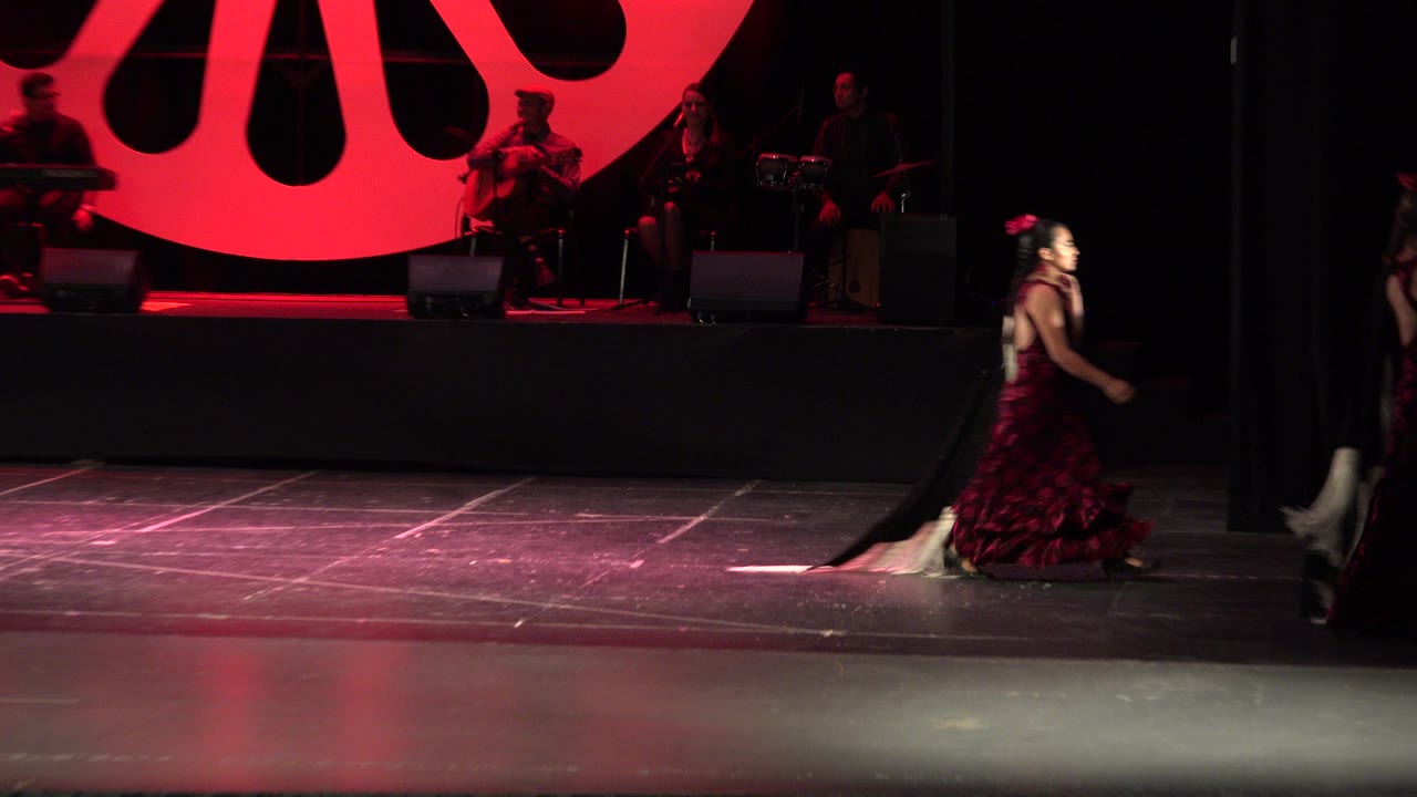 At 0:01 in Cabo San Lucas, Mexico, the performer is nearer the right side of the frame while the red circular light and band remain in the background.