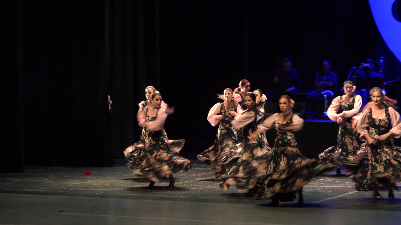 Women in floral dresses dancing on a dark stage.