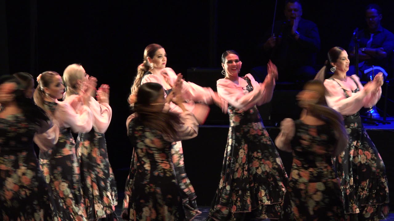 Women clap and turn in coordinated floral stage costumes.