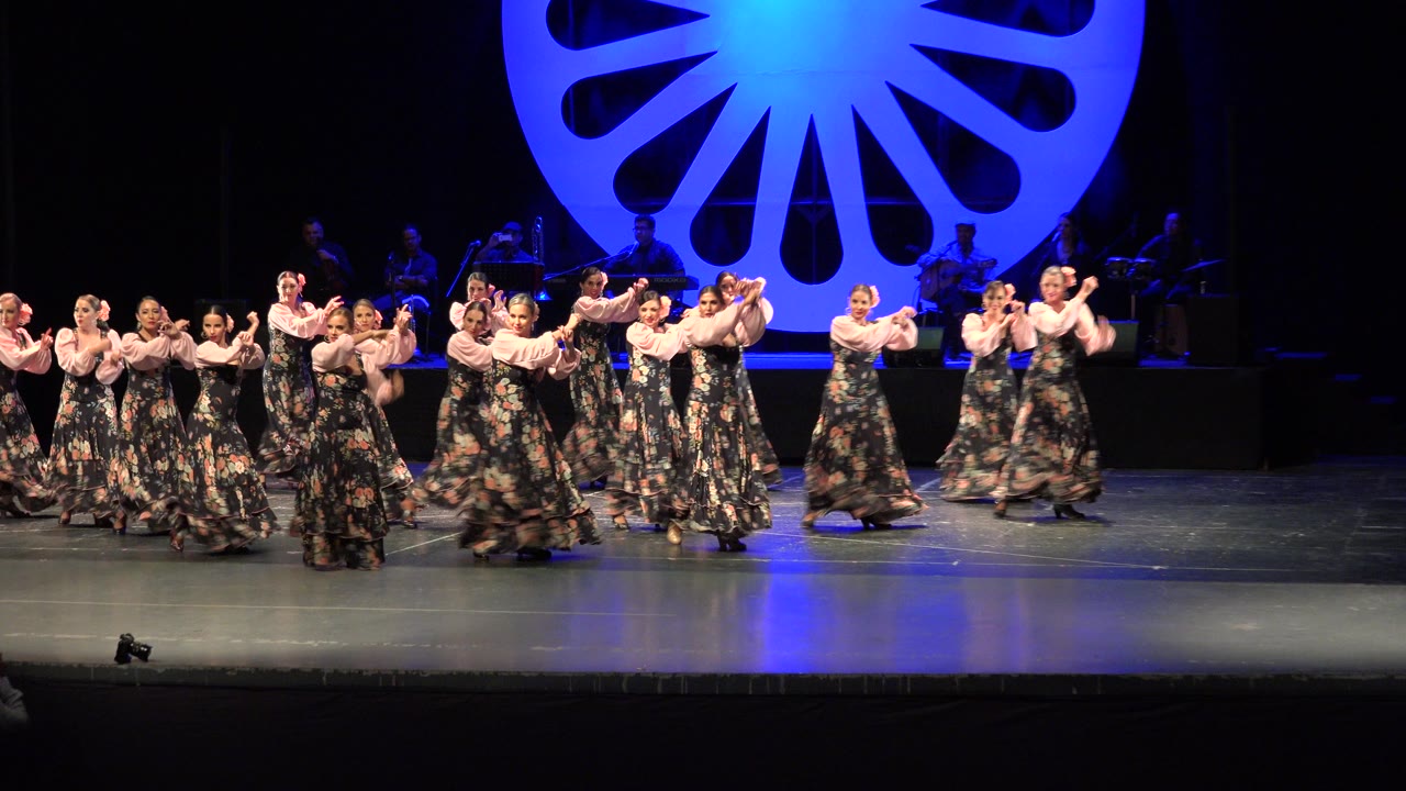 Women in floral dresses dancing on a stage with blue backdrop
