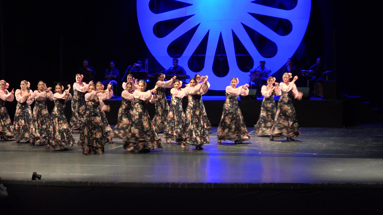 The dancers remain spread across the Cabo San Lucas stage, with several pairs turning while the blue-lit circular set piece fills the upper background.