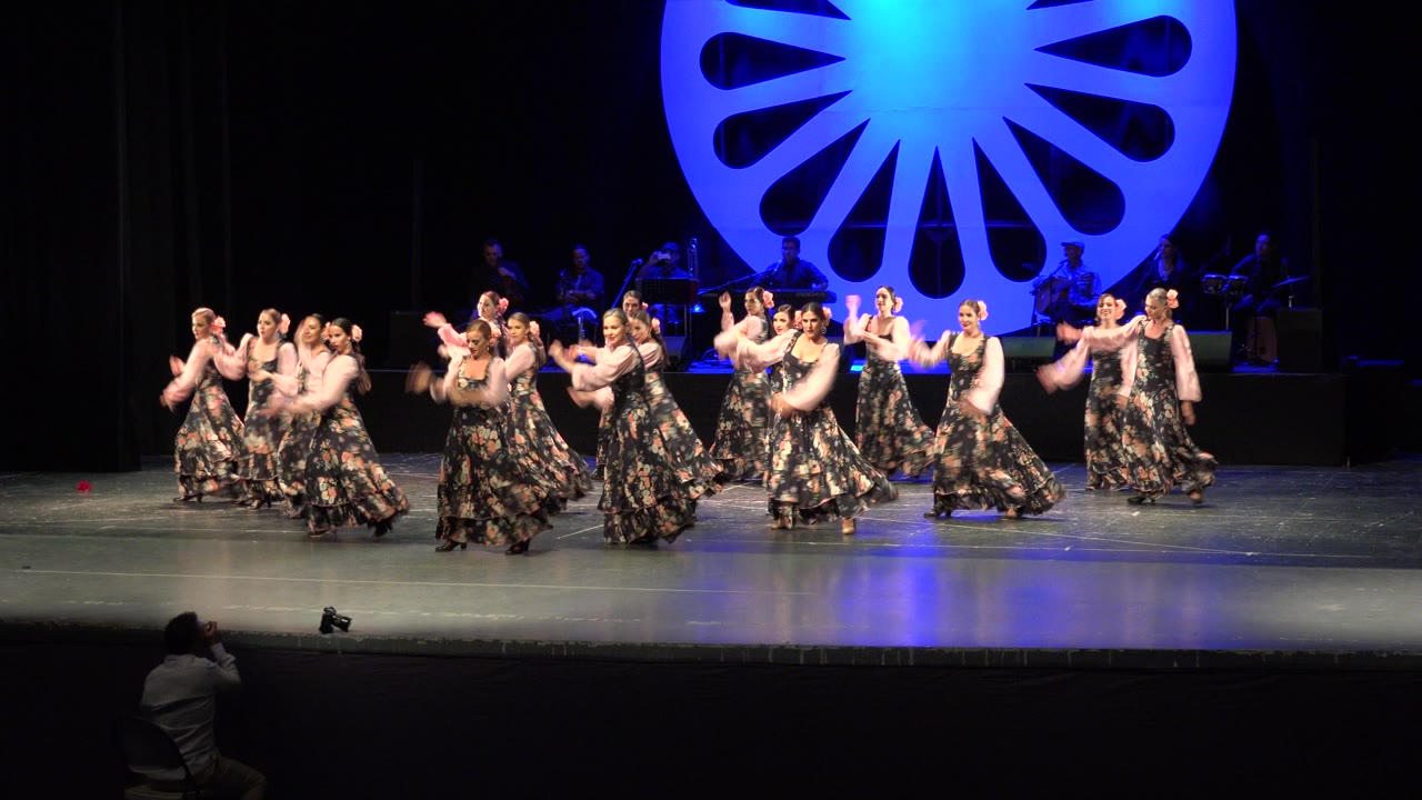 Group of young women dancing on a stage with a blue circular backdrop.