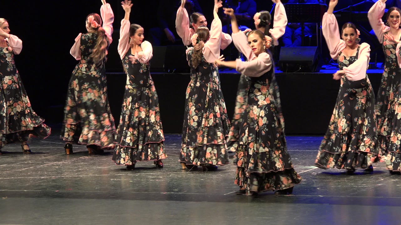 The dancers shift positions across the Cabo San Lucas stage, with several women facing inward while one performer near the front turns toward the camera.