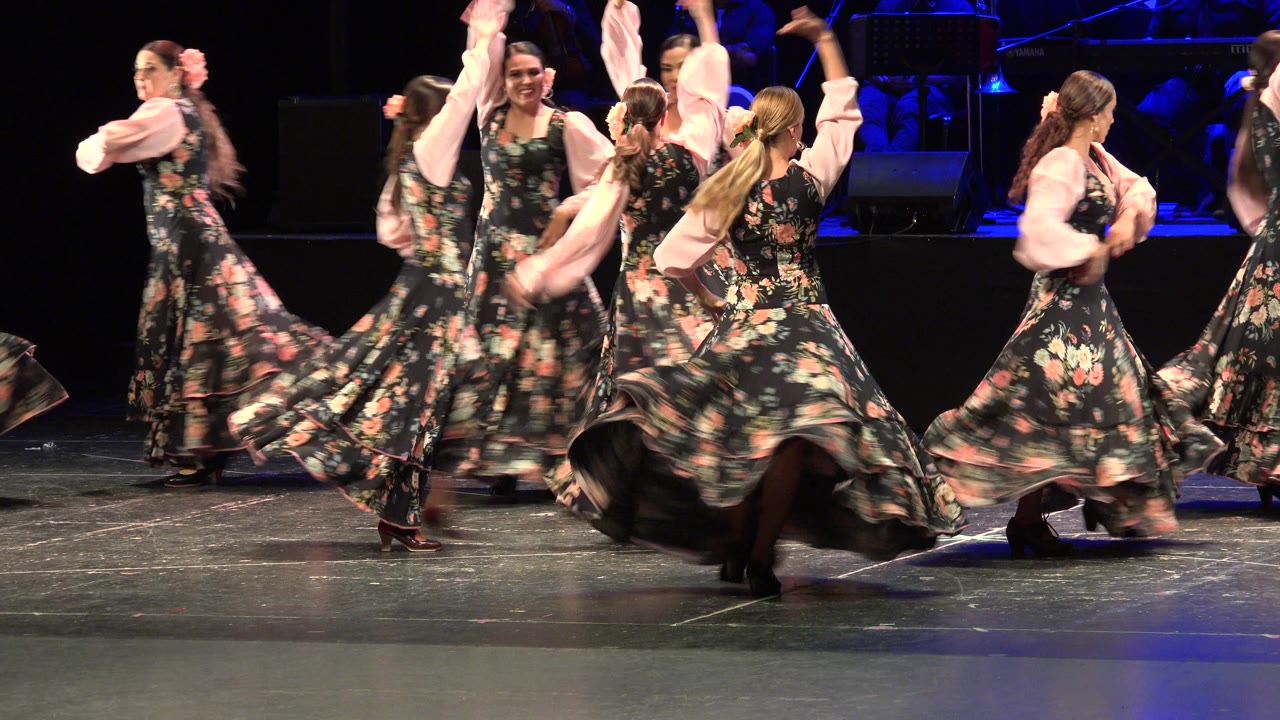 Women in floral dresses dancing on a dark stage