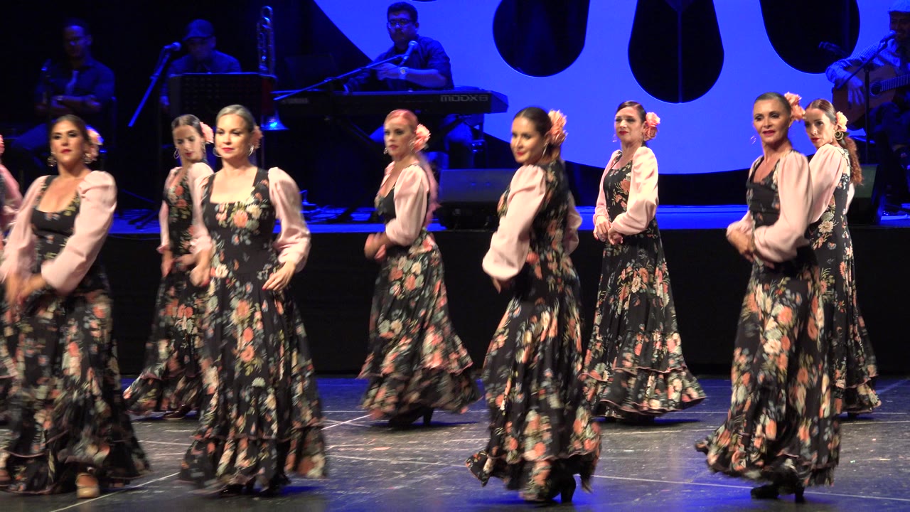 Women in floral dresses dancing on a blue-lit stage.