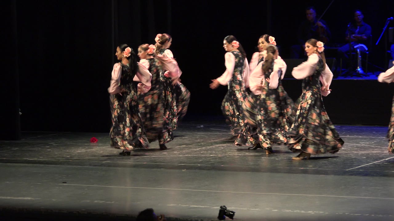 Dancers in floral dresses crossing a dark stage.