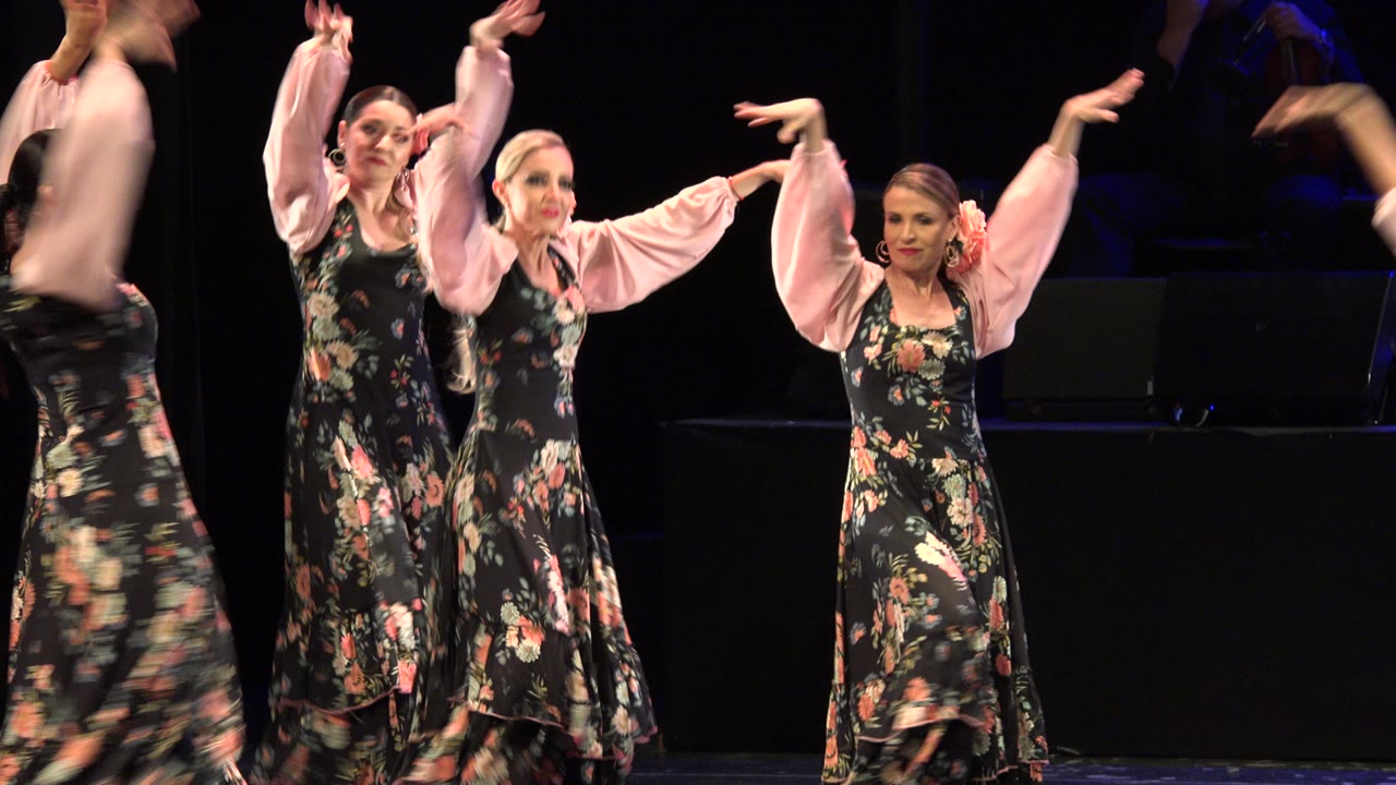 Dancers move across the stage with arms extended and skirts turning.