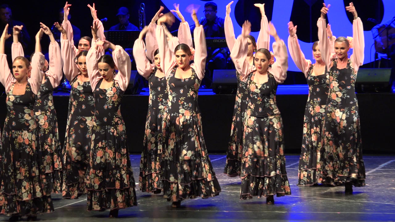 Women dancers transition from raised arms on stage.