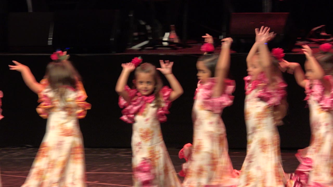 Several young girls turn across a stage in matching floral costumes.