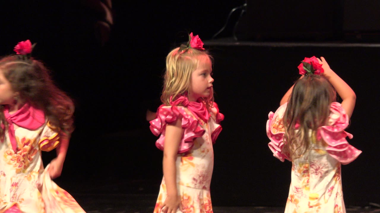 Girl in a floral dance dress raises an arm beside other children.