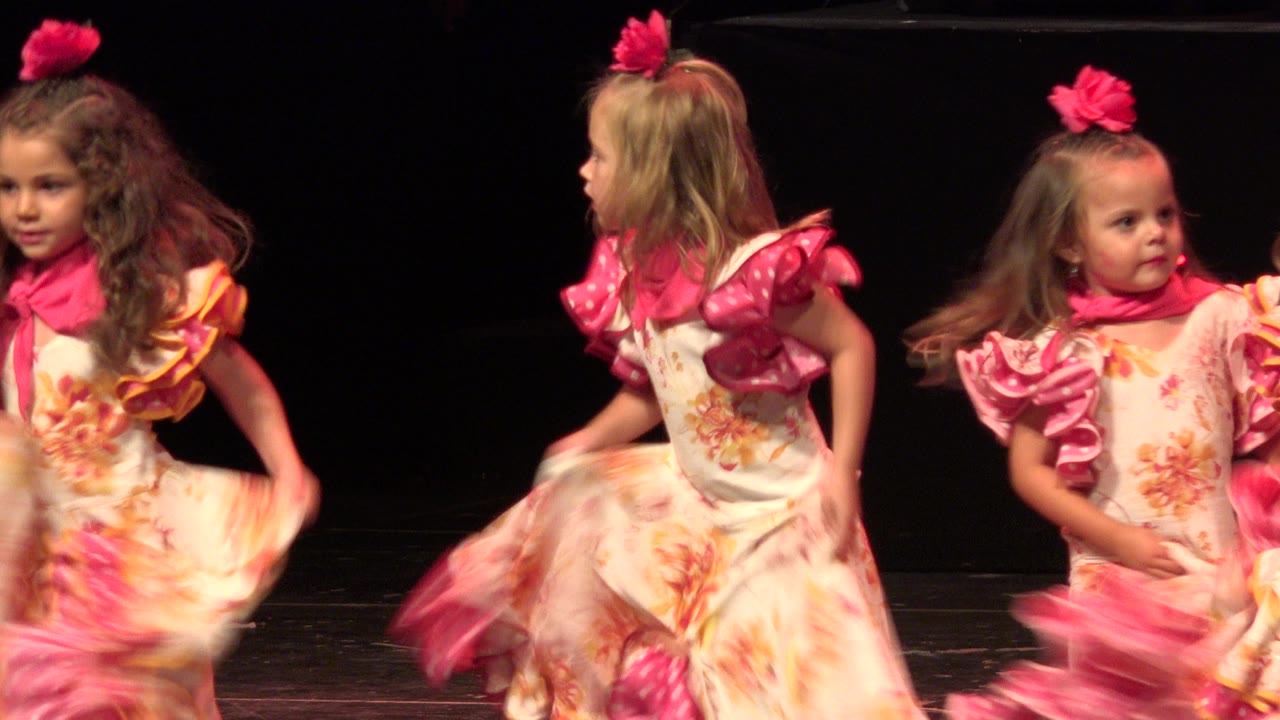 Girls in matching pink and floral costumes dance under stage light.