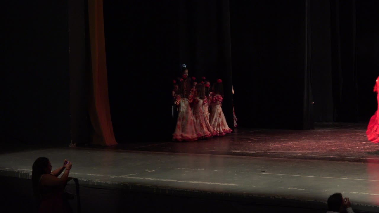Dancers wait at stage left as a red-costumed performer enters from the right.
