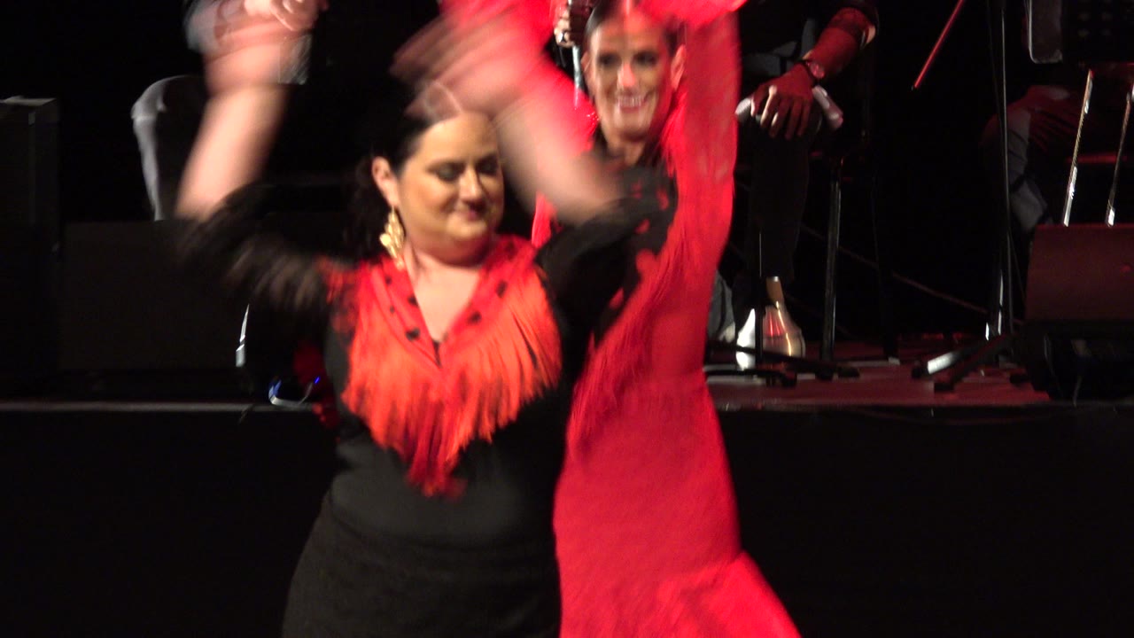 Adult woman in black and red dance costume raising her arms on a dark stage.