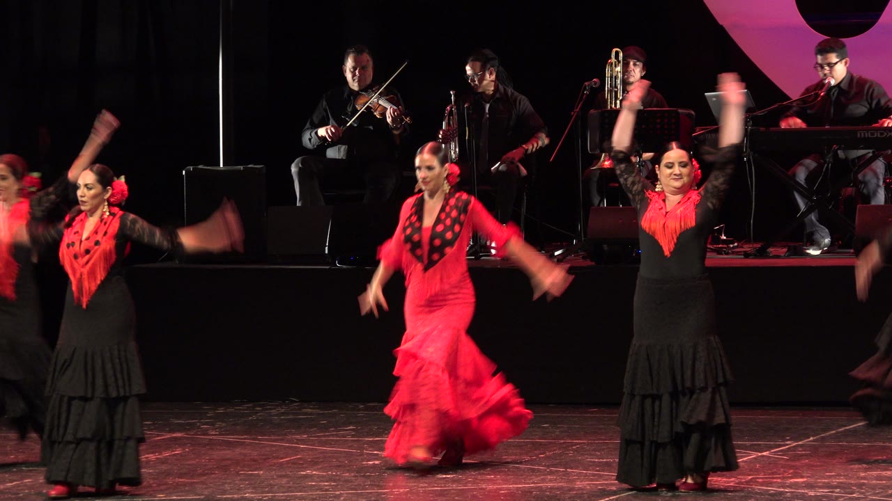 Women perform with raised arms while musicians play behind them on stage.